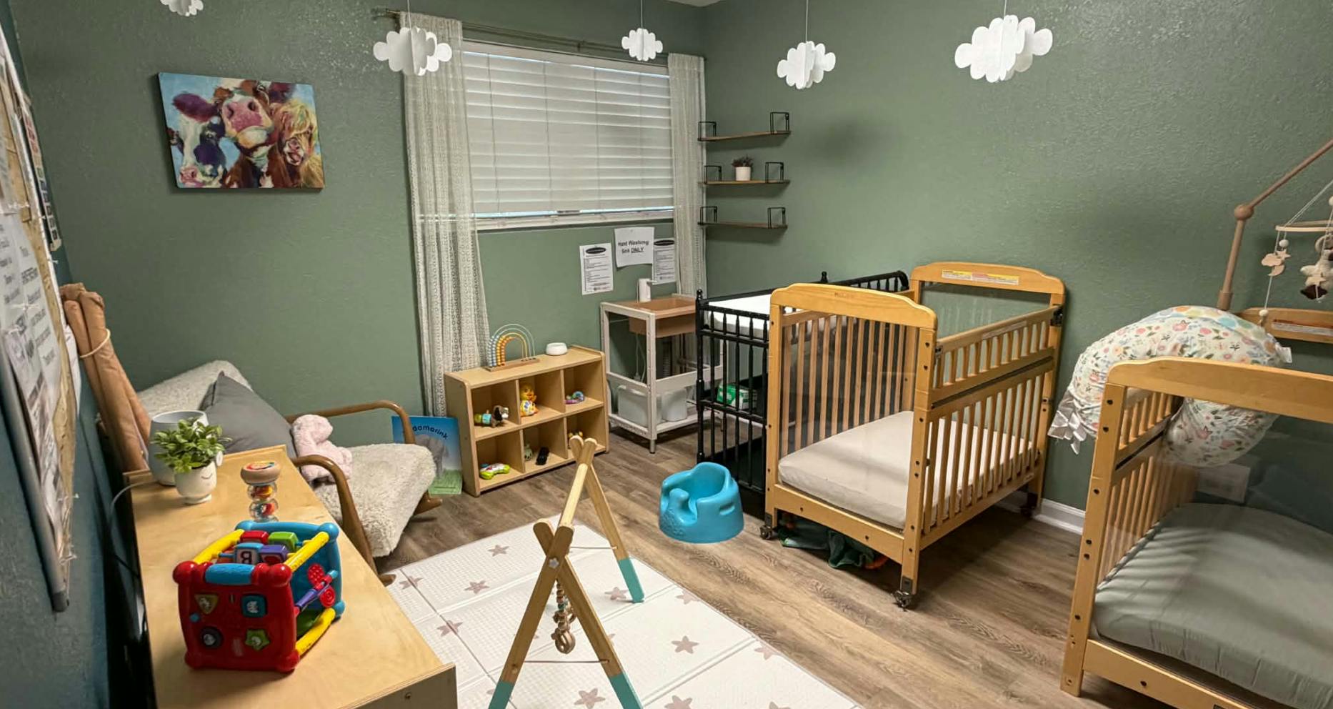 Childcare room with wooden cribs, toys, and green walls