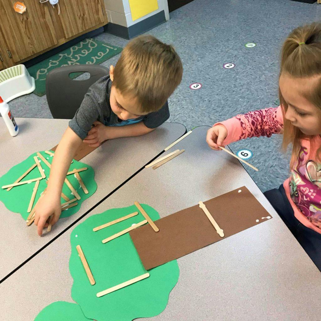 Two children working on crafts with popsicle sticks and paper cutouts