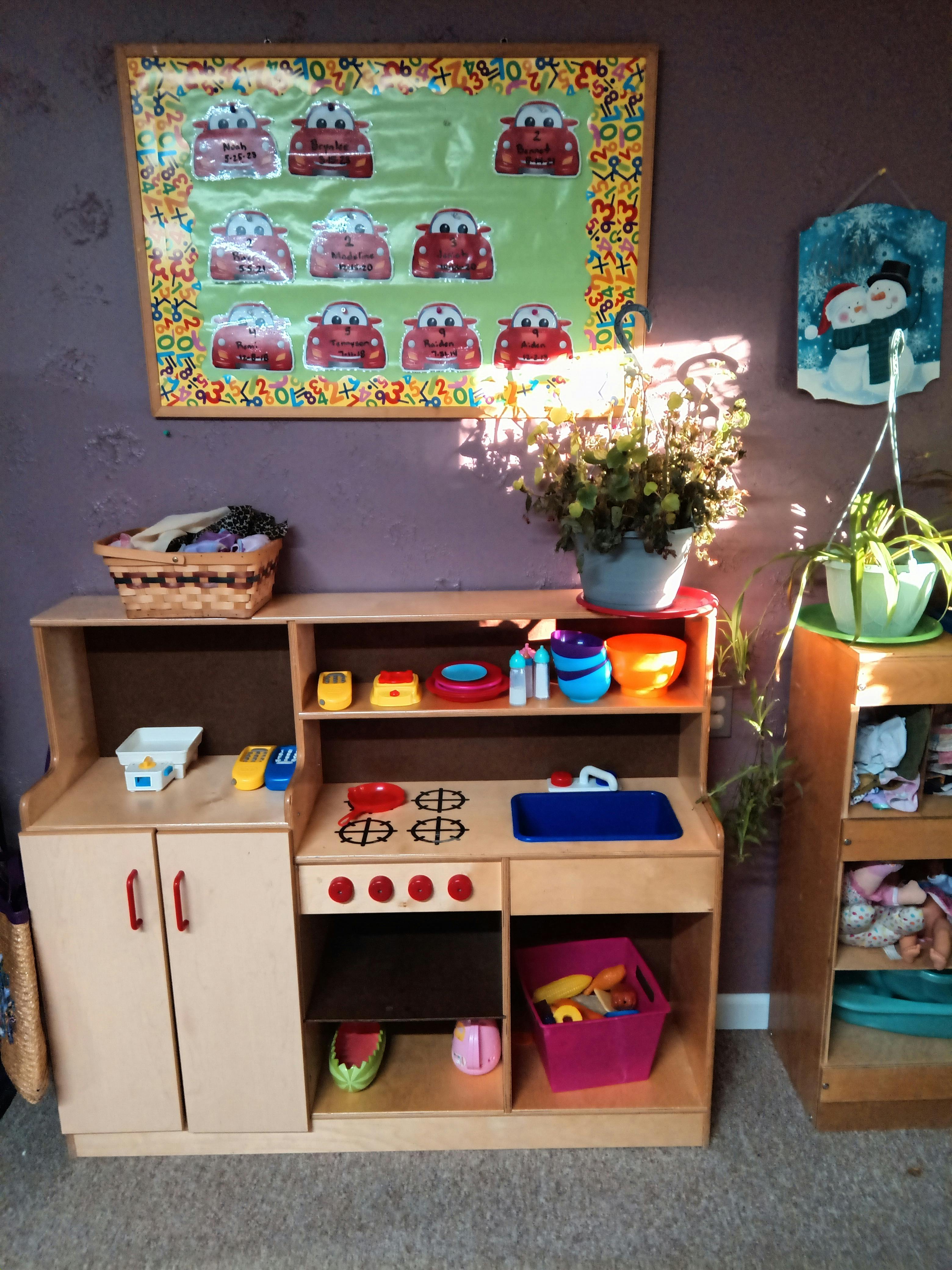 Play kitchen with toy dishes and food, a basket, and plants