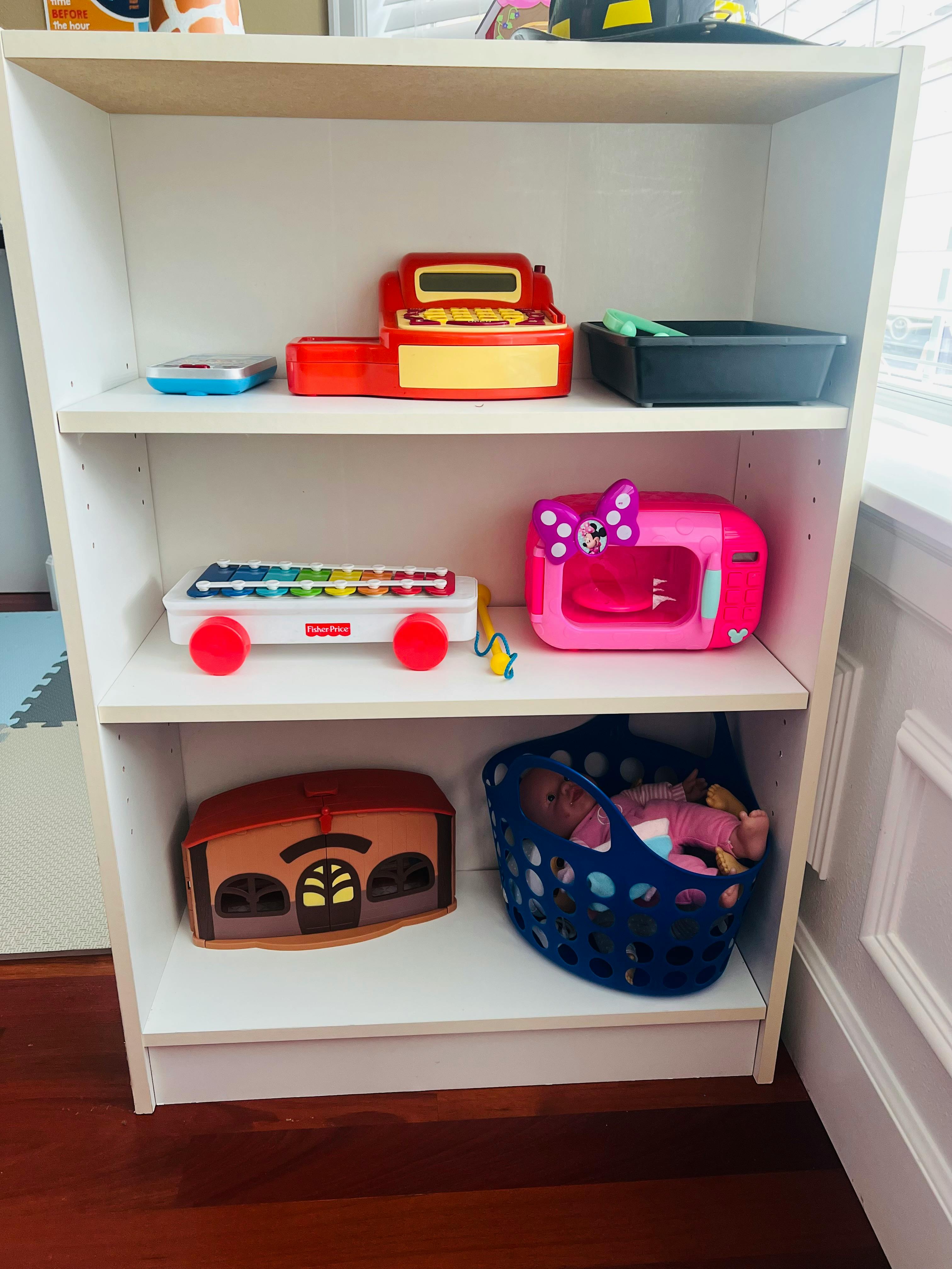 Shelf with various toys including a cash register, xylophone, and doll