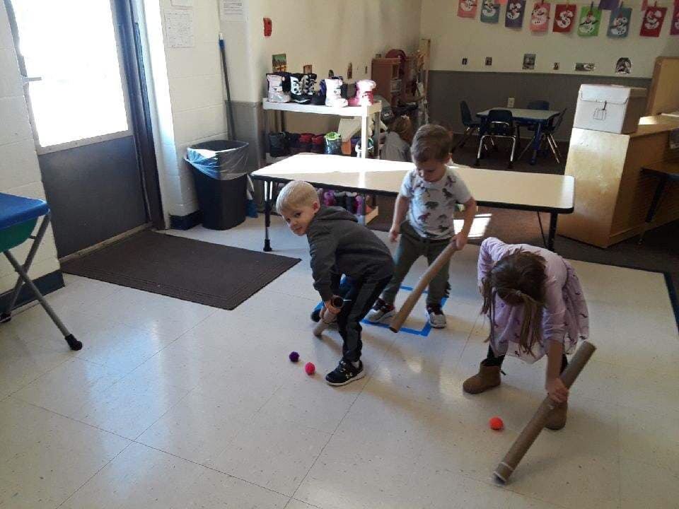 Three children playing with sticks and small balls indoors