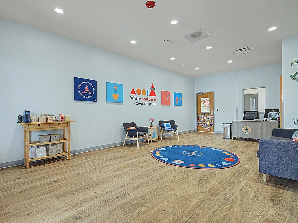 Room with light blue walls, wooden floor, a rug, chairs, and a reception desk