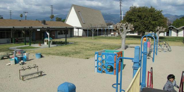 Child on playground equipment with buildings and trees in background