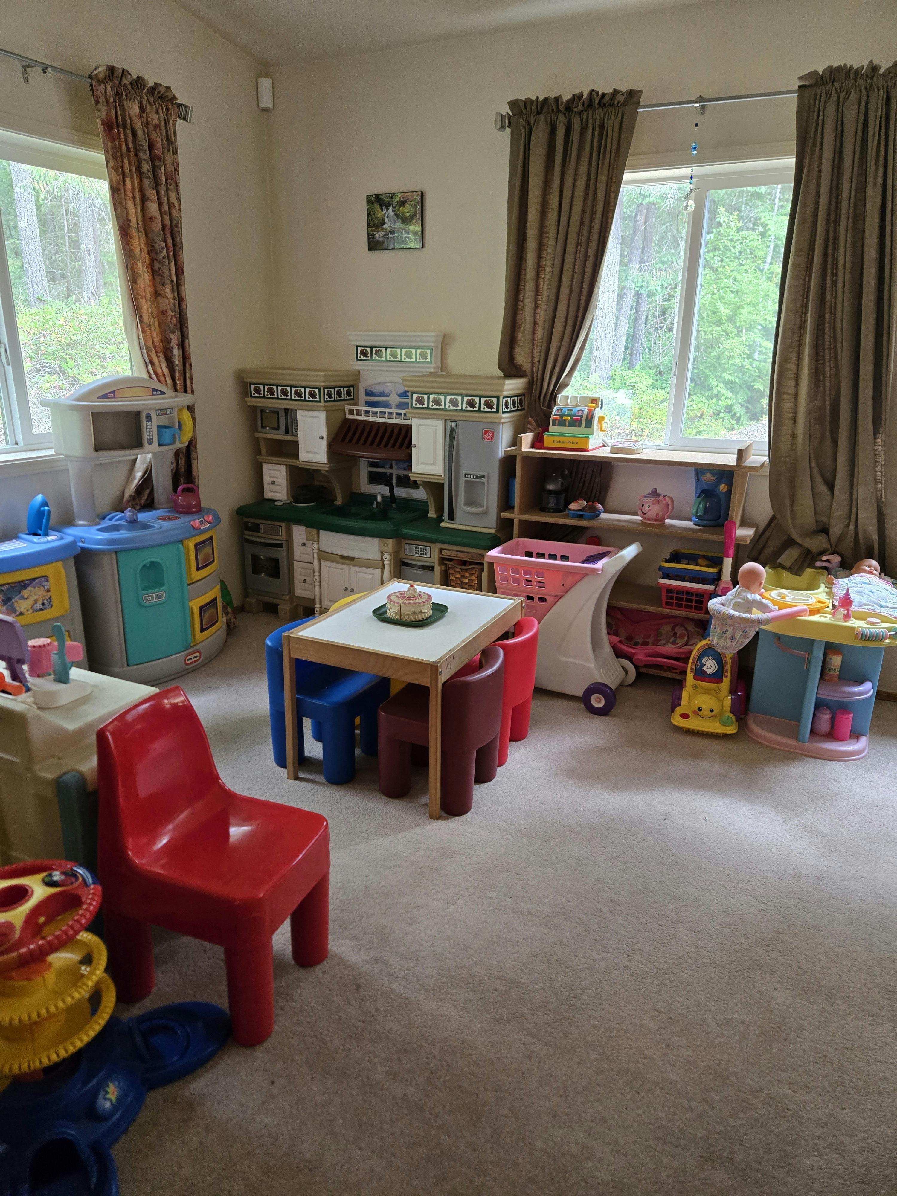 Playroom with multiple plastic toy kitchens, a table, and small chairs