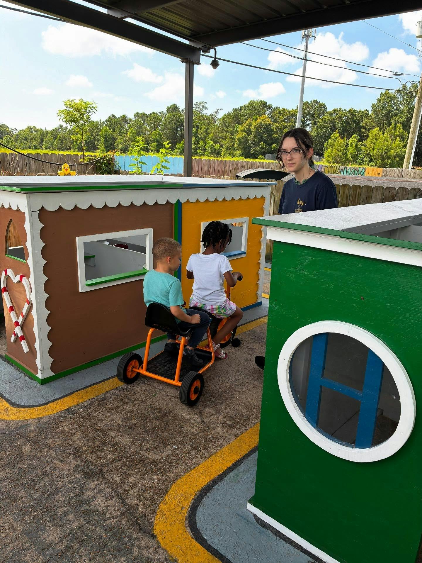 Two children on ride-on toys with a person standing behind them