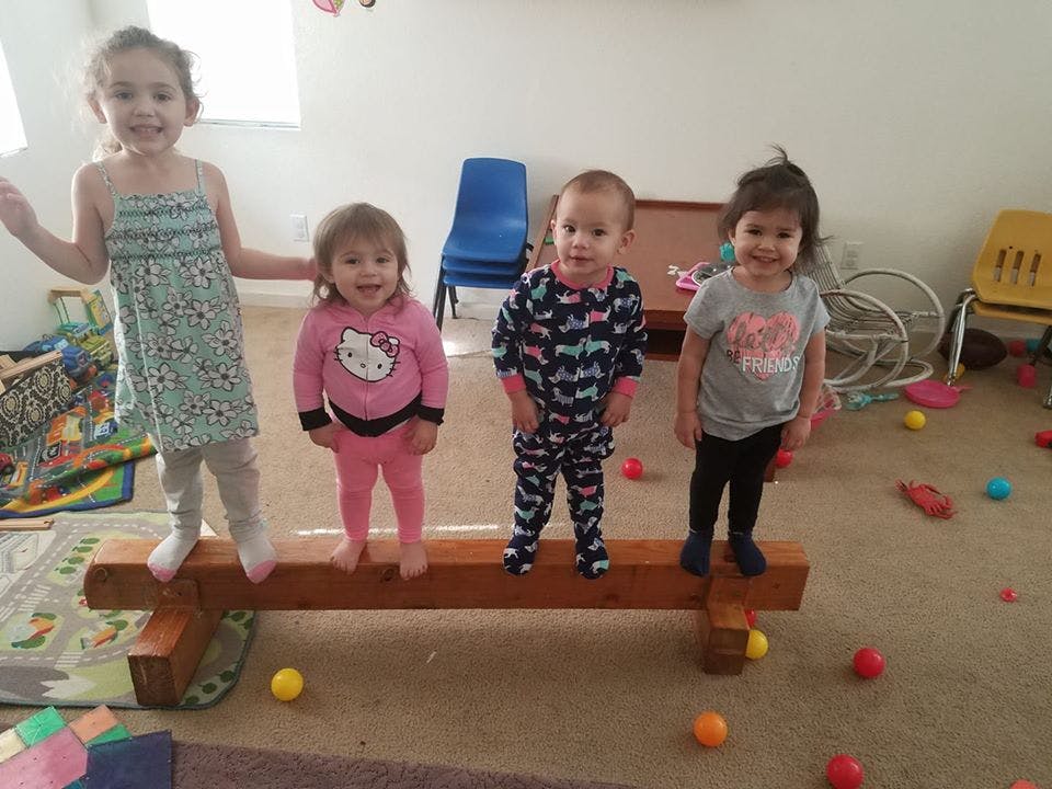 Four children standing on a wooden balance beam indoors