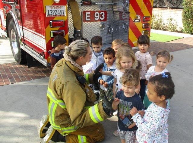 Firefighter kneeling and talking to a group of children in front of a fire truck