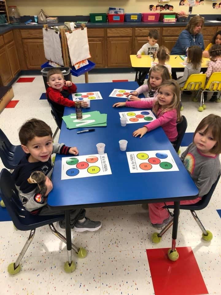 Children sitting at a blue table in a classroom