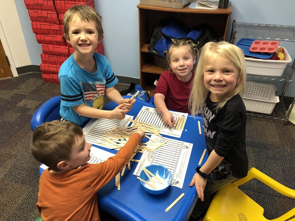 Four children at a table making crafts with craft sticks