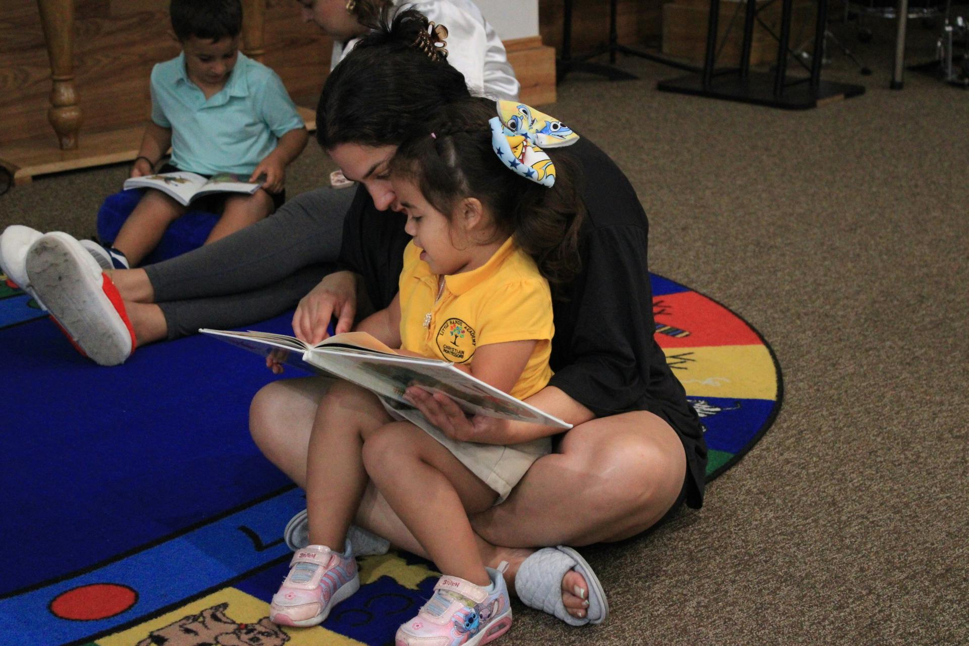 Person and child sitting on floor reading a book