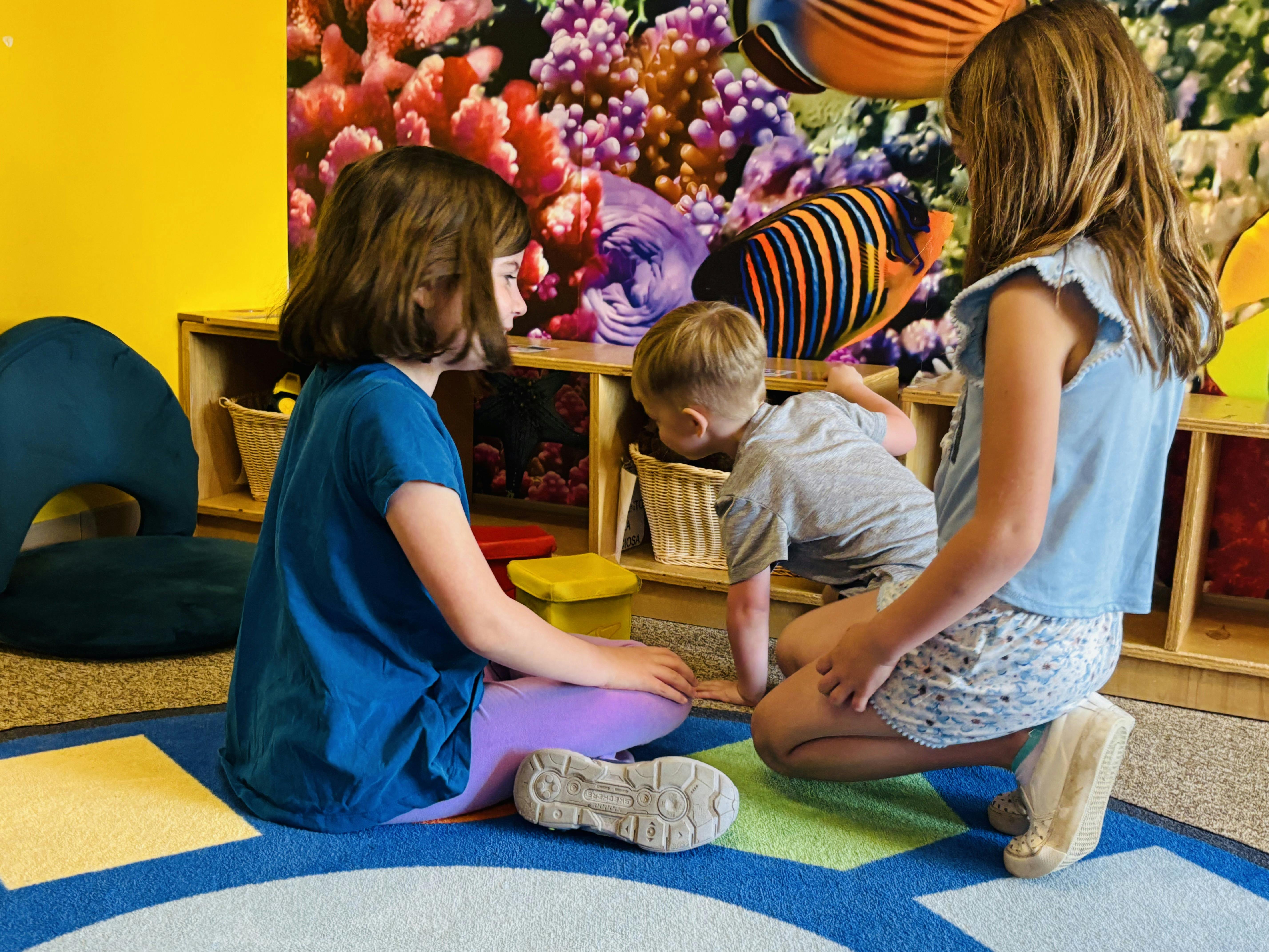 Three children playing on a rug in a room