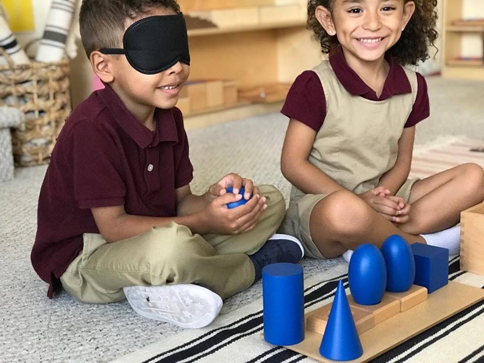 Child with blindfold holding a blue object, child sitting next to them