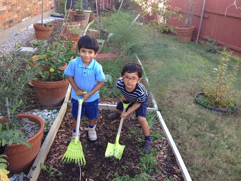 Two children holding a rake and a shovel in a garden bed