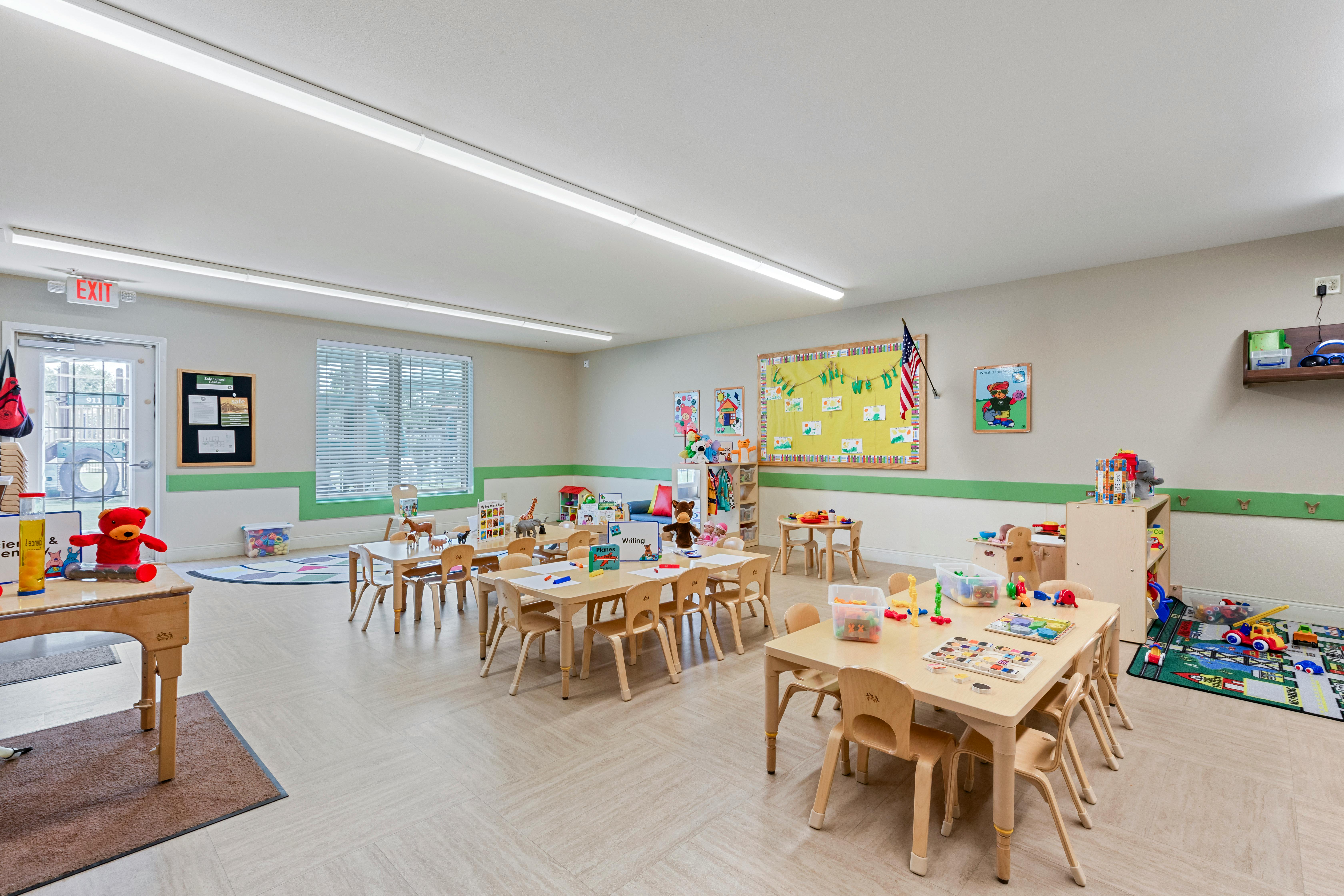 Classroom with multiple wooden tables and chairs, toys, and educational posters