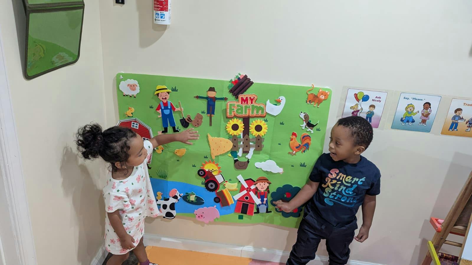 Two children pointing at a My Farm felt board in a classroom