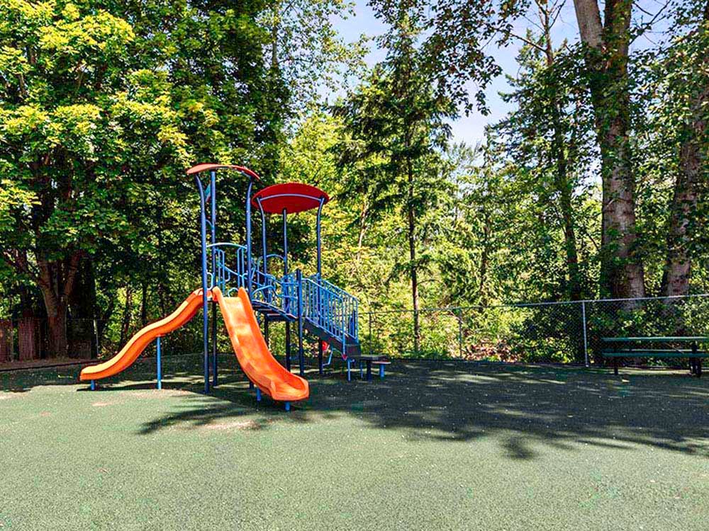 Playground structure with two orange slides on a green ground cover