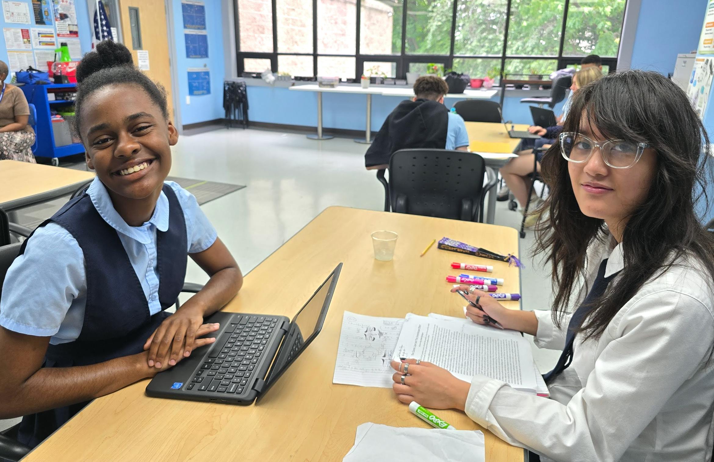 Two people at a table with a laptop and papers in a classroom