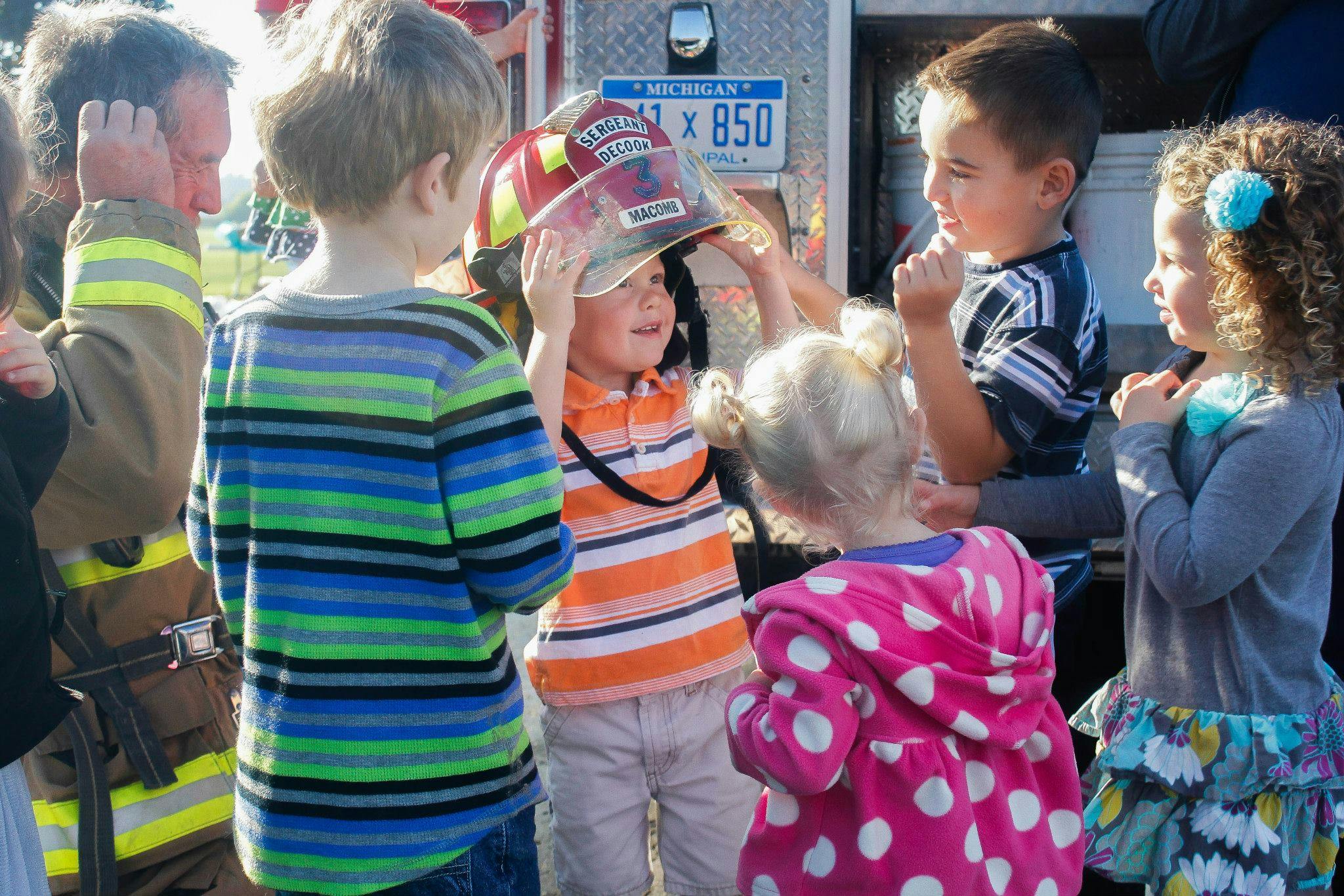 Children gathered around a person in a firefighter uniform, one child wearing a helmet