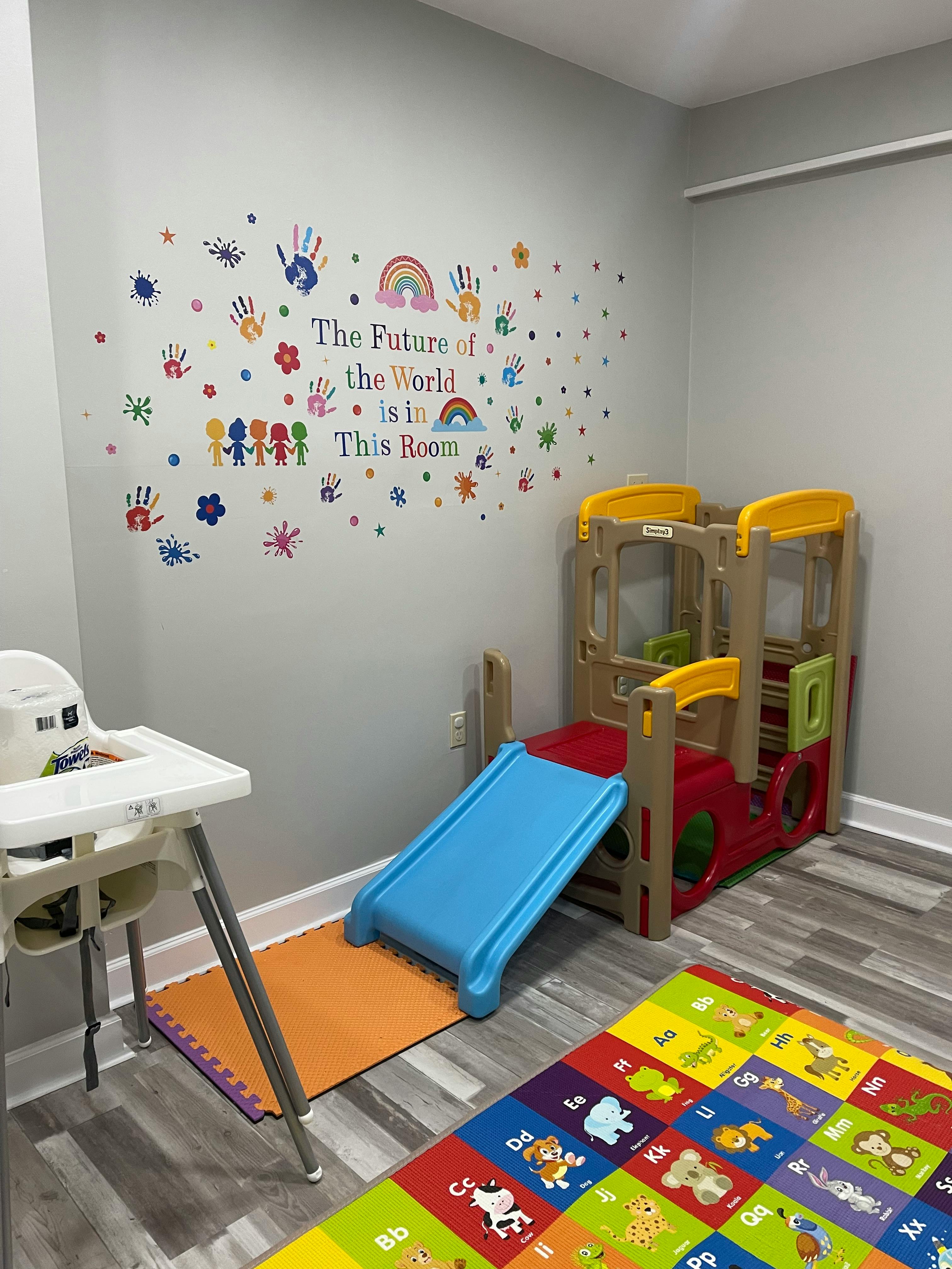 Indoor play area with a slide, high chair, and wall decals with colorful decals