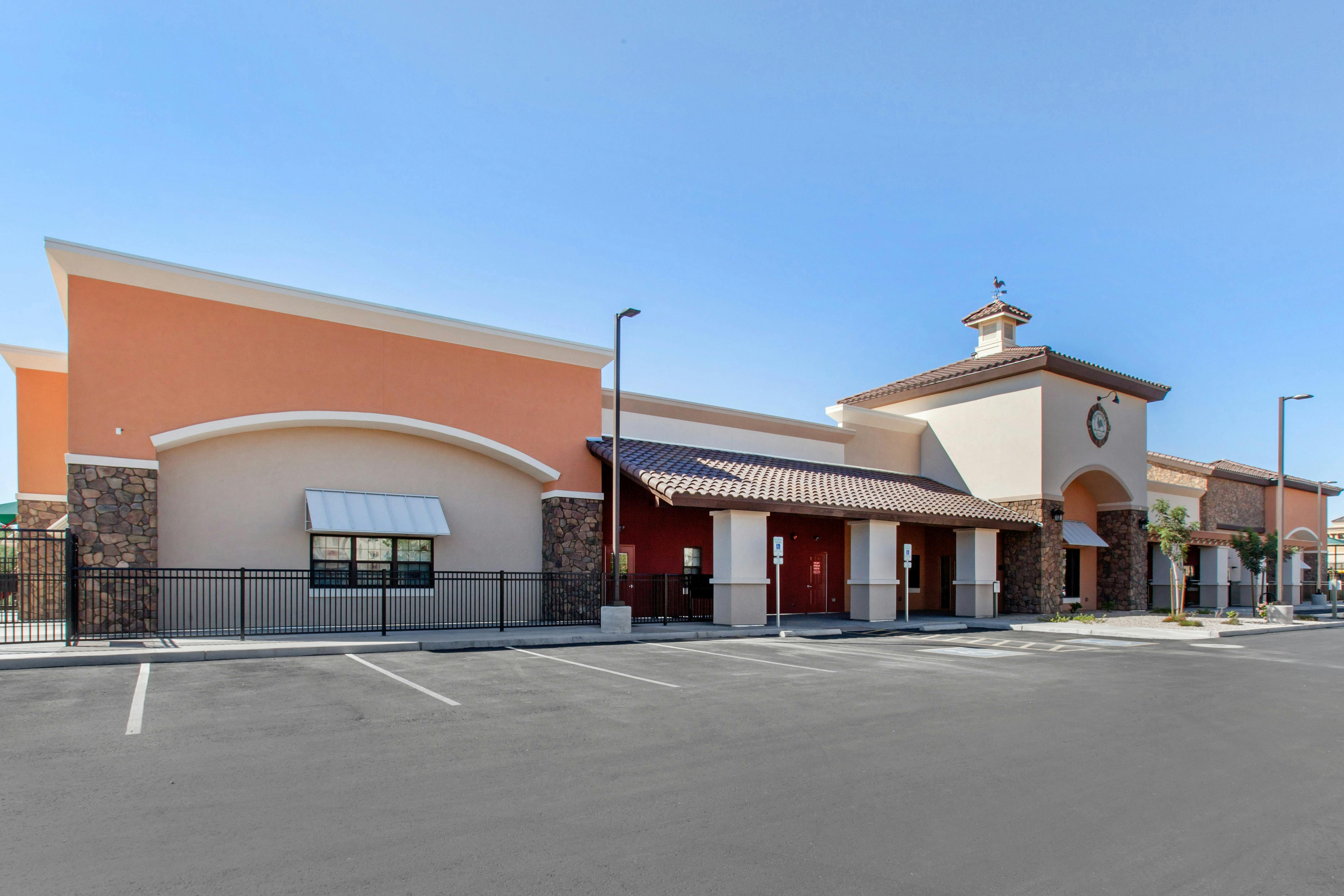 Exterior view of a building with peach and beige walls, a tiled roof, and a parking lot