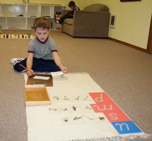 Child sitting on floor with pencil and paper, another child on a couch