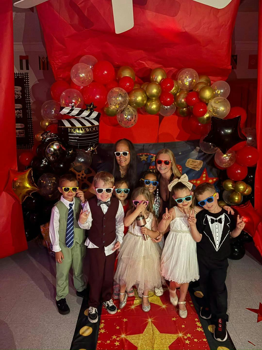 Group of children and adults wearing sunglasses at a red carpet themed event