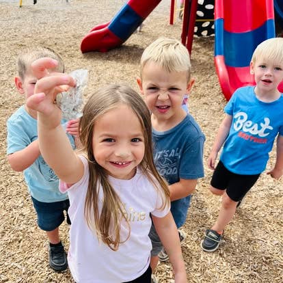 Four children on a playground, one child holding up a small object