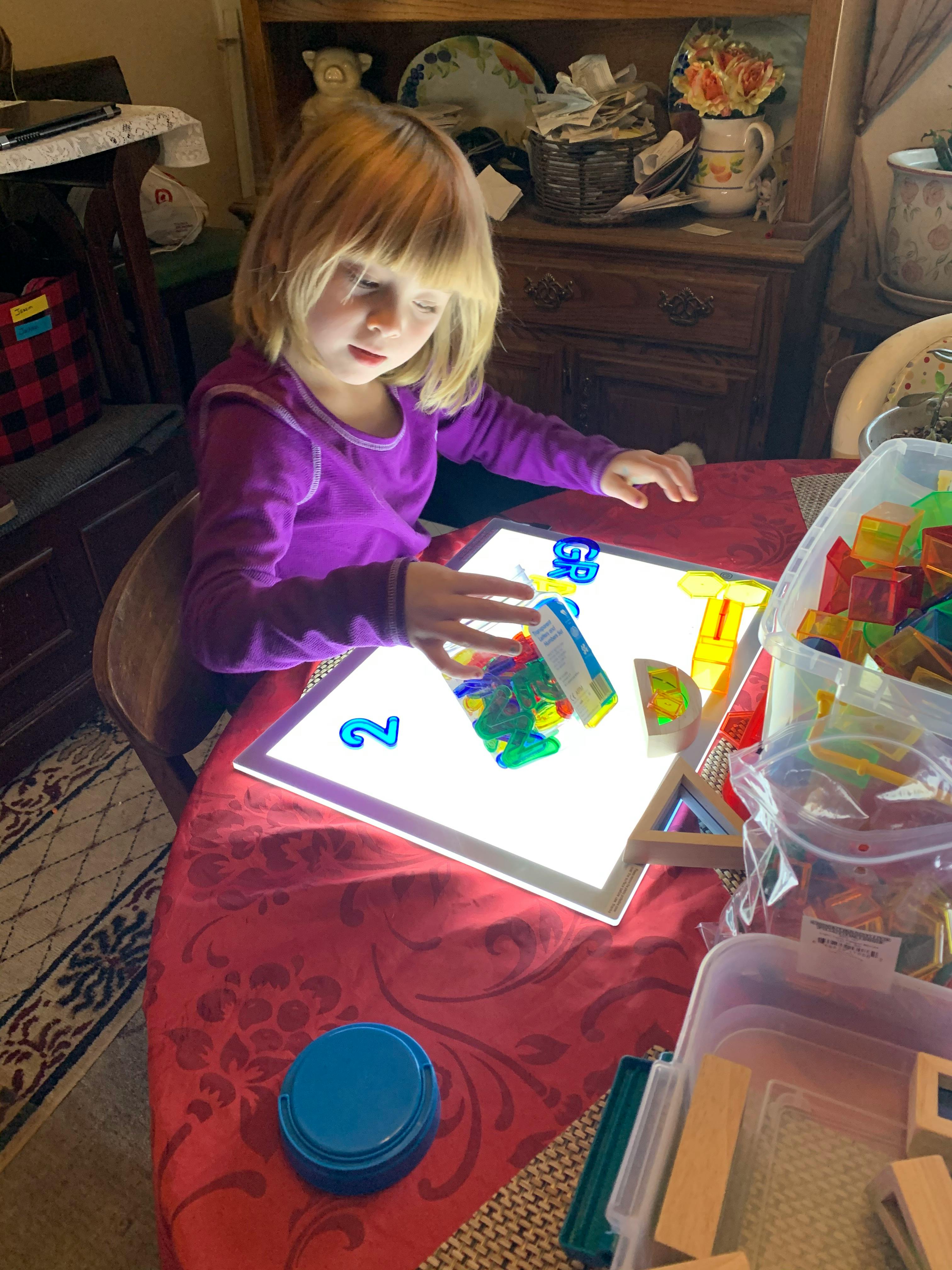 Child playing with colorful translucent shapes on a light-up board