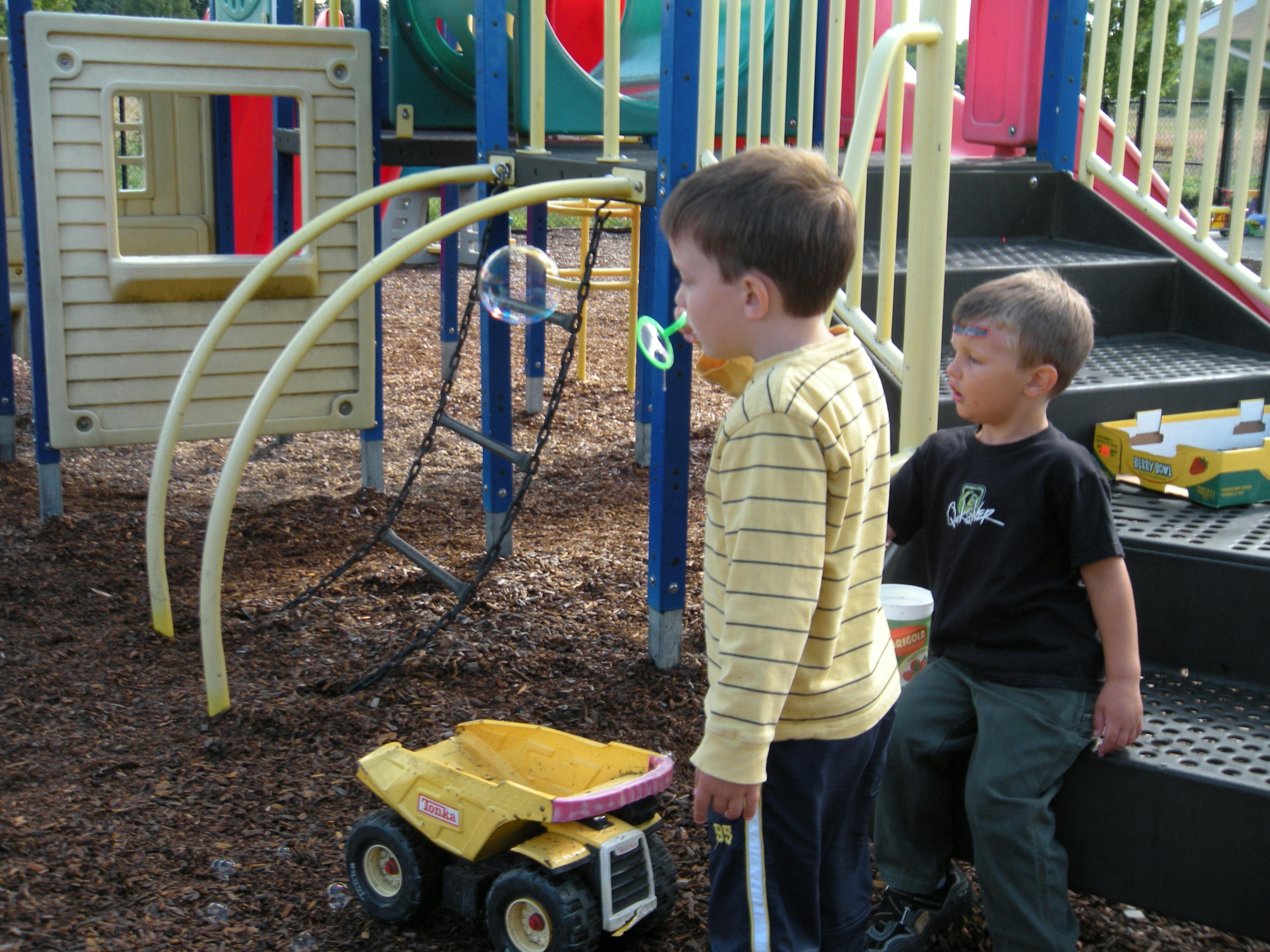 Two children on a playground with a toy truck