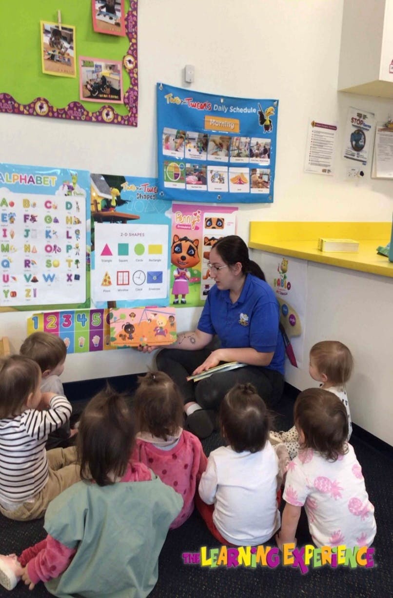 Person reading a book to a group of children in a classroom
