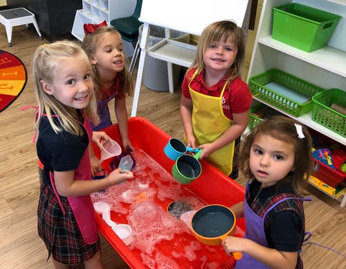 Children playing with water and bubbles in a red sensory bin