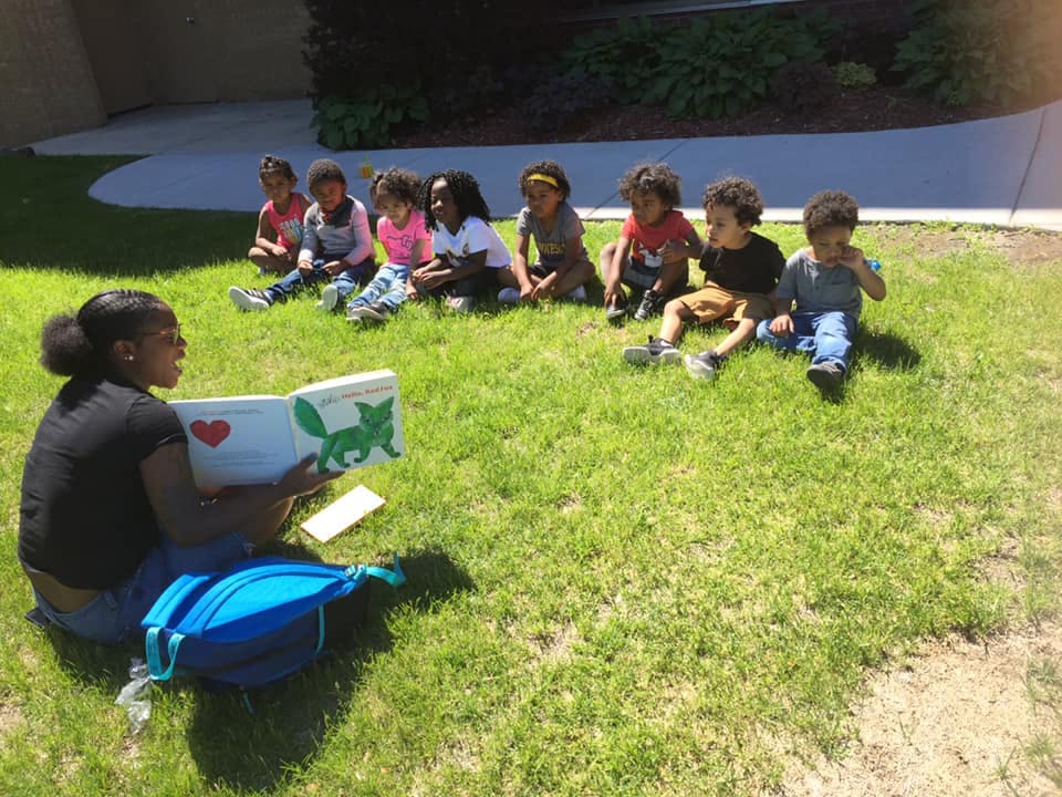 Person reading a book to a group of children sitting on grass