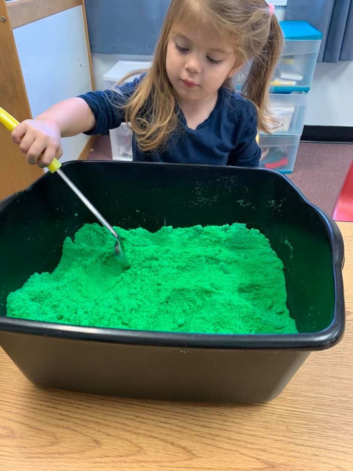 Child playing with green kinetic sand in a black bin