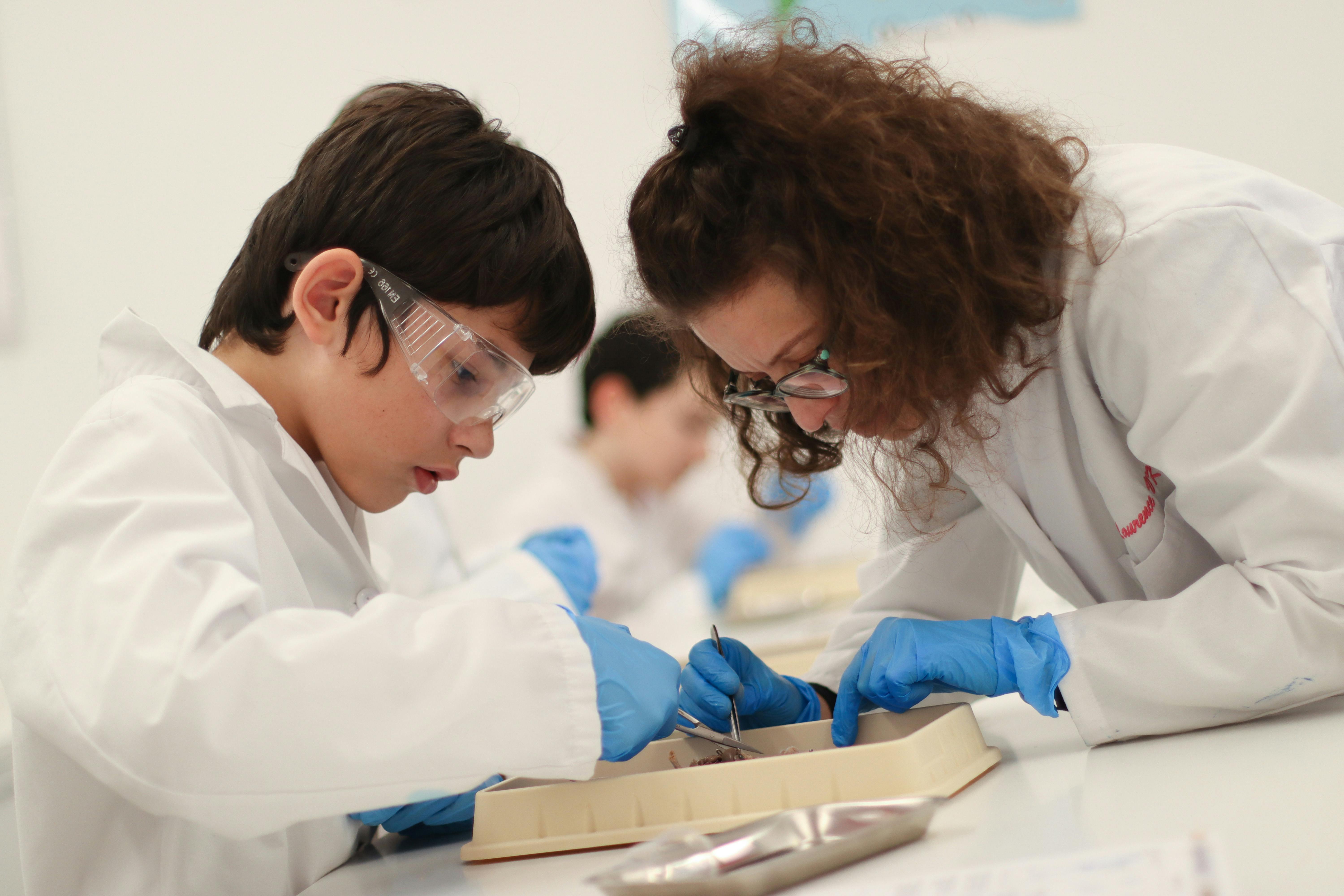 Two people in lab coats and safety glasses working with tools