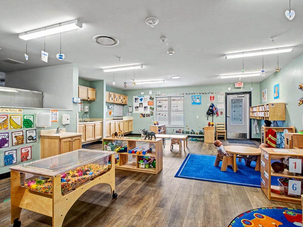 Classroom with wooden tables, play structures, and a child sitting at a table