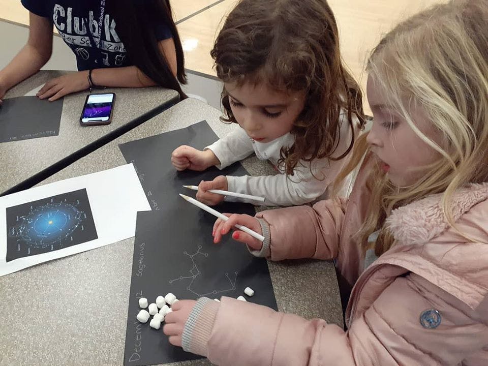 Two children drawing on black paper with white pencils
