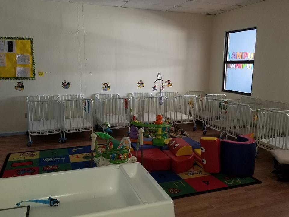 Room with multiple cribs, a colorful rug, and play equipment