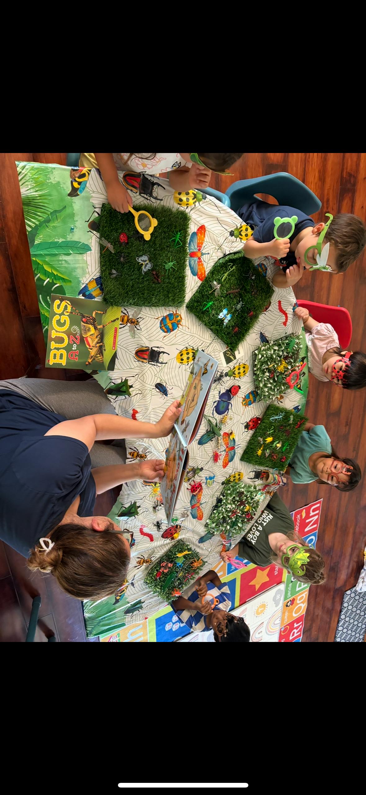 Group of children observing toy insects with magnifying glasses at a table