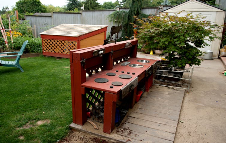 Outdoor play kitchen with a wooden dog house and green lawn in a backyard
