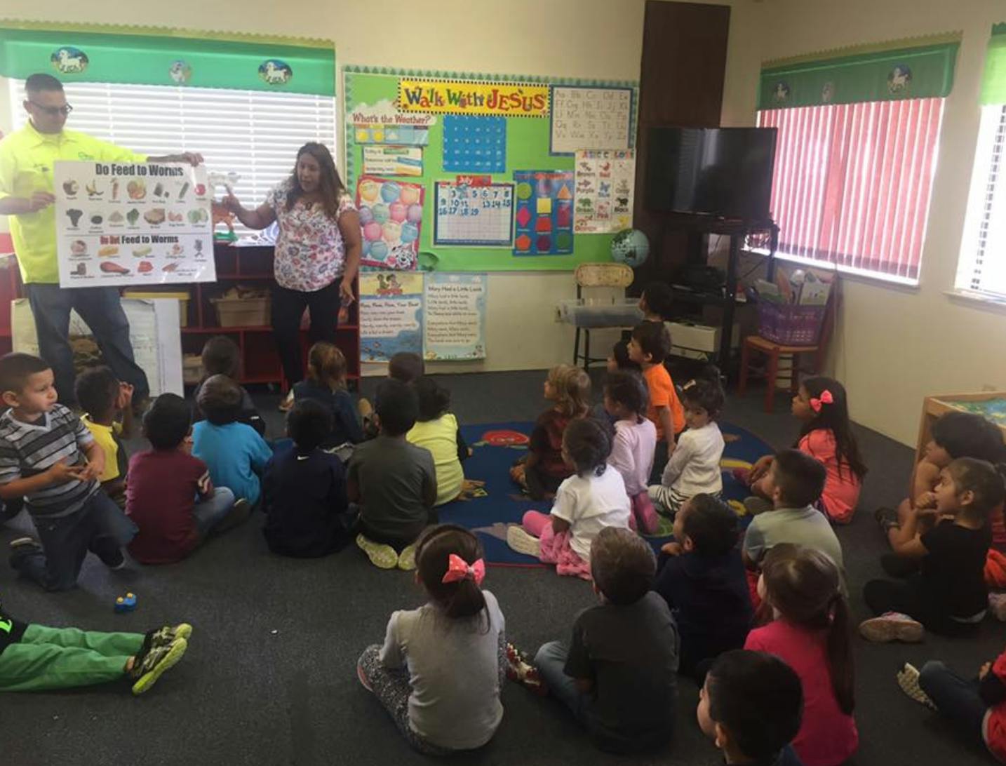 Two adults presenting a poster to a group of children in a classroom