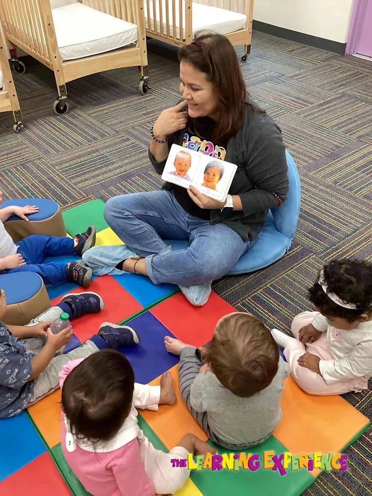 Person sitting on floor showing a book to children in a group of children
