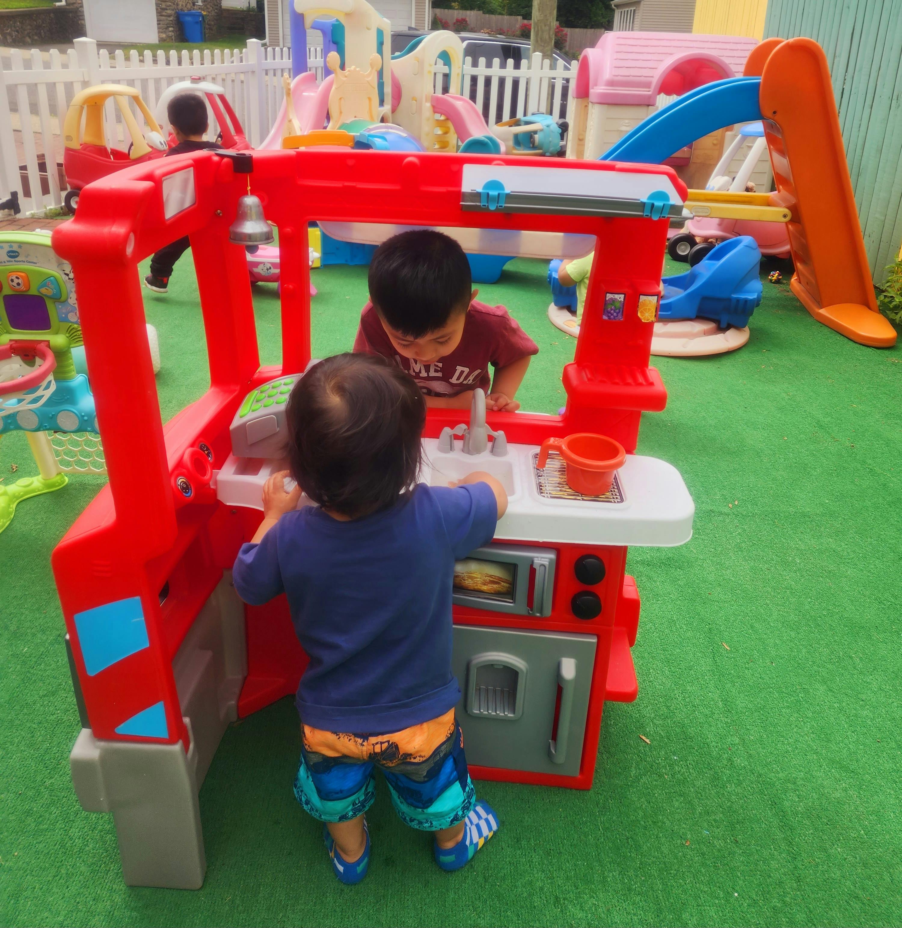 Two children playing with a toy kitchen set outdoors