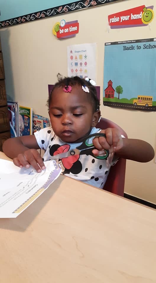 Child cutting paper with scissors at a table