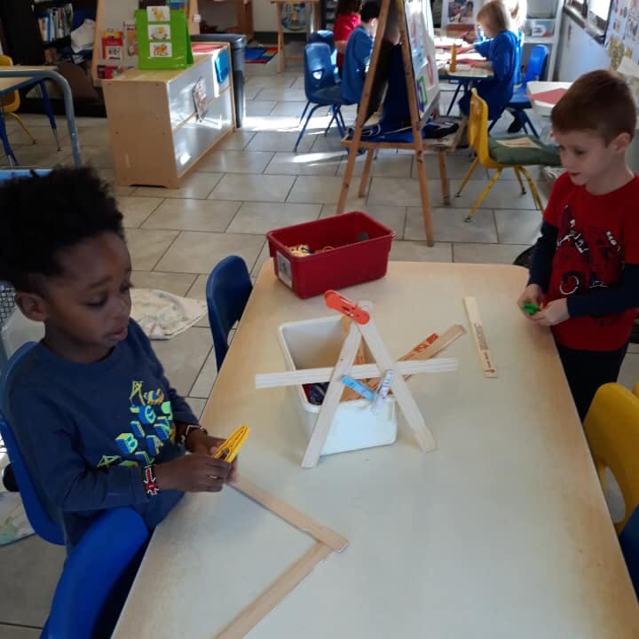 Two children playing with craft sticks and clothespins at a table in a classroom