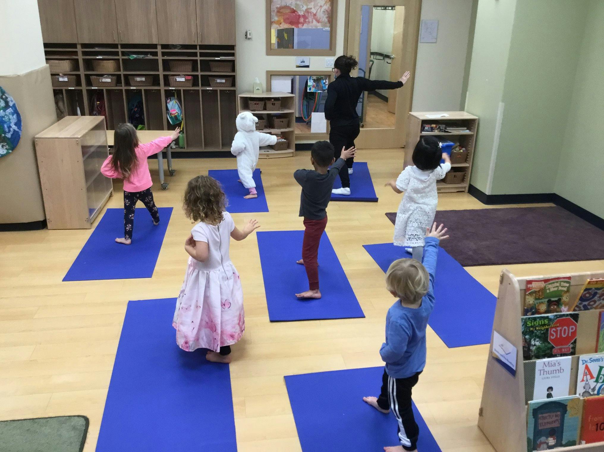 Children and an adult doing yoga poses on blue mats in a classroom