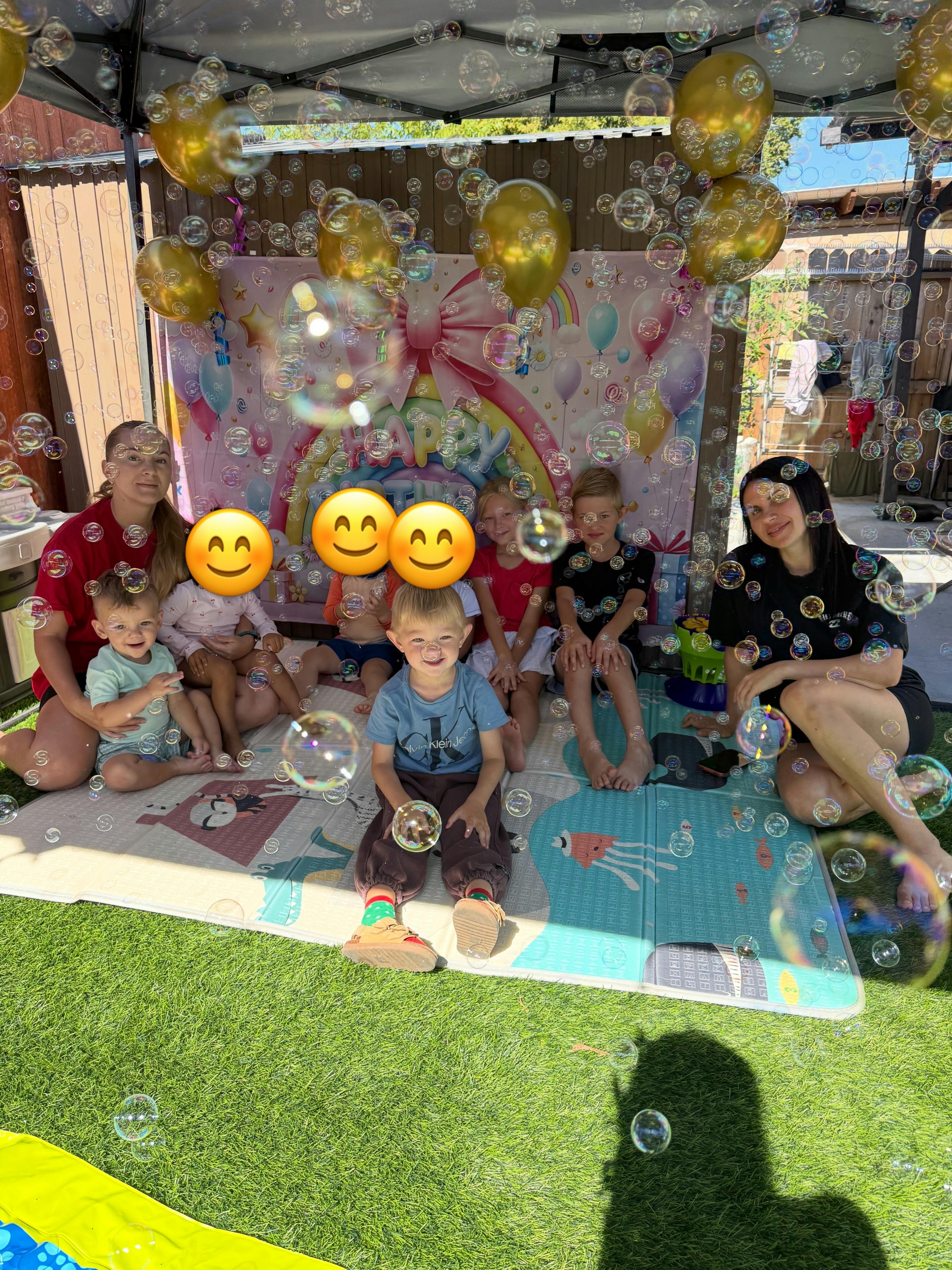 Group of children and adults sitting in front of a birthday backdrop with bubbles