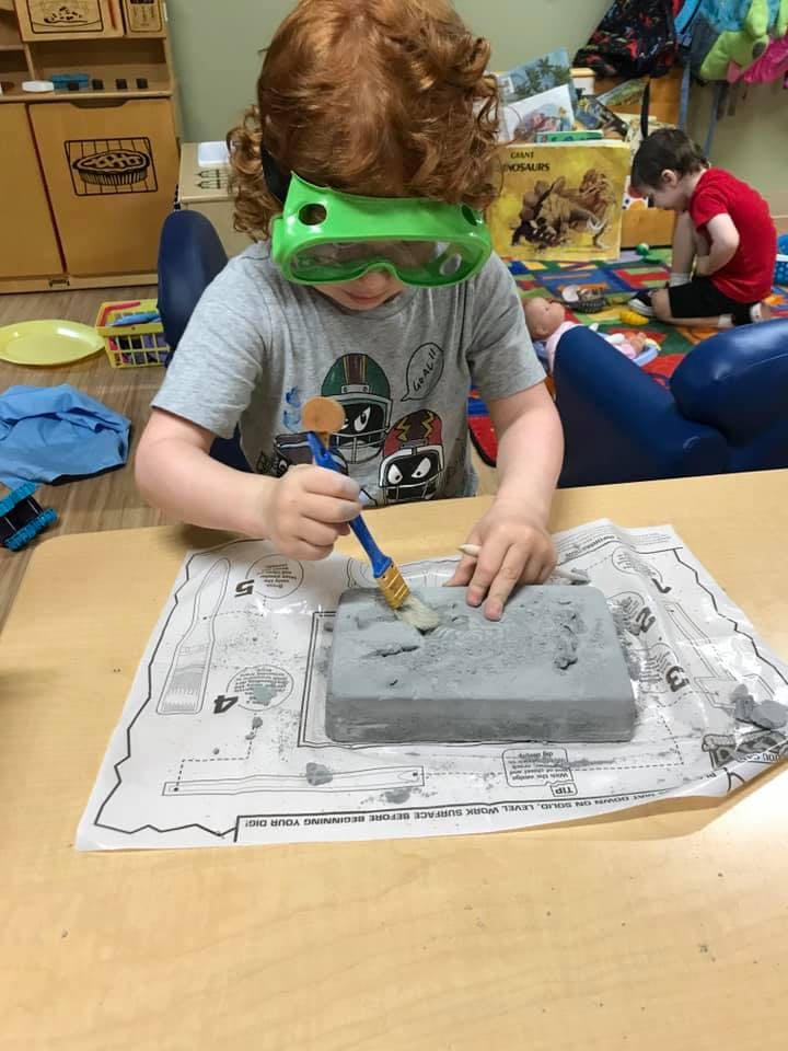 Child wearing green safety goggles and brushing a gray block
