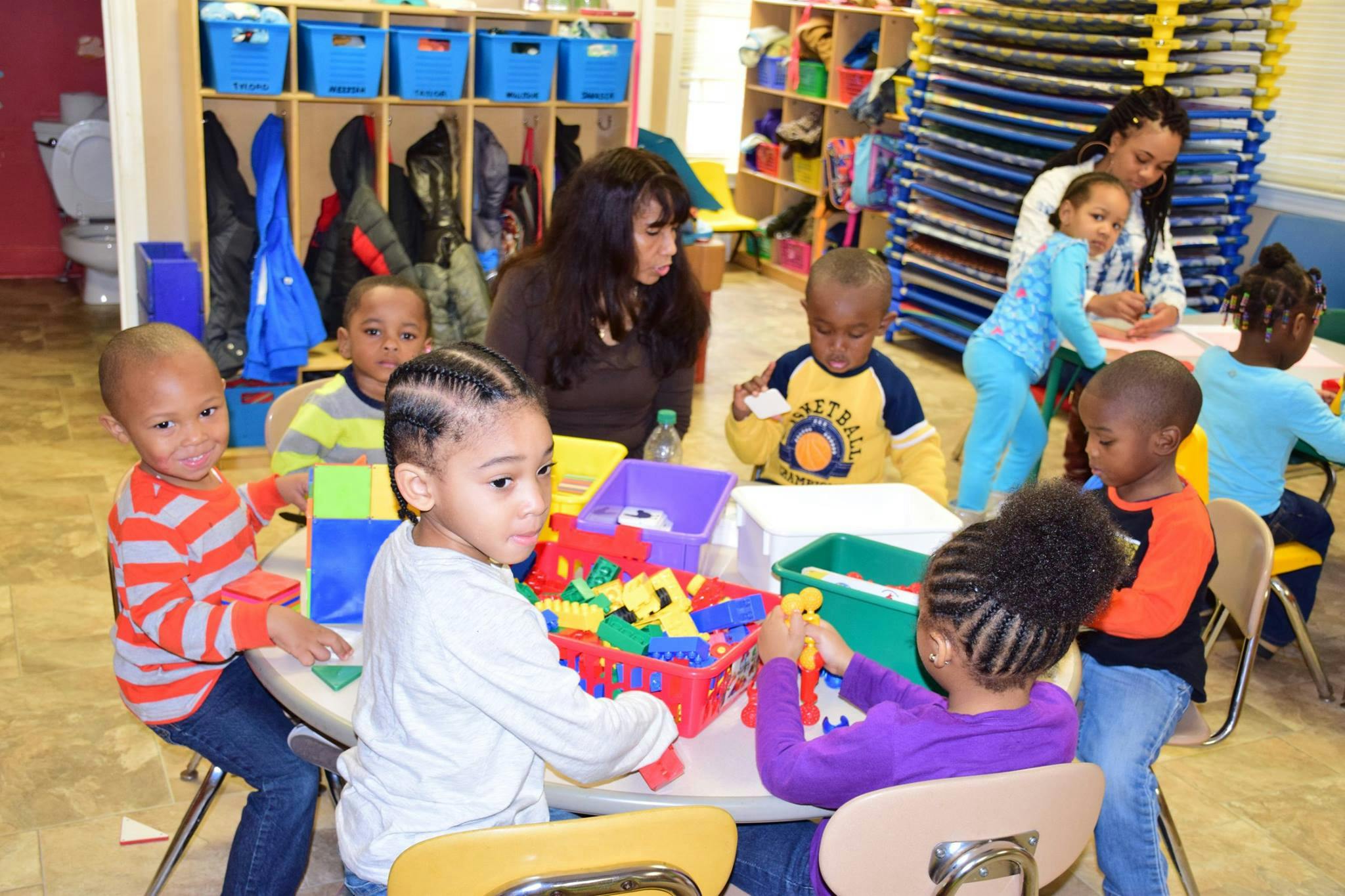 Adults and children playing with toys at a table in a classroom