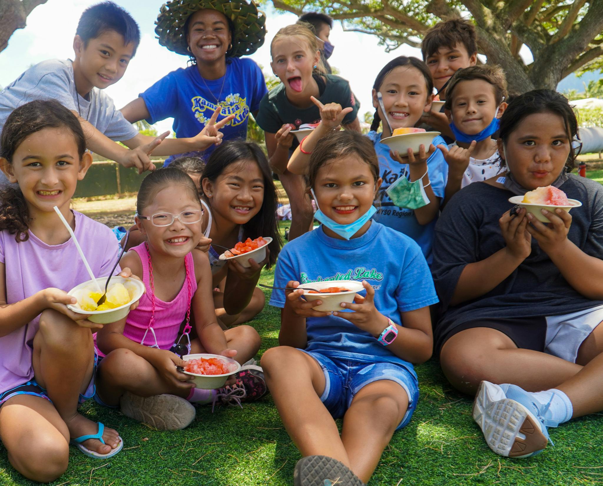 Group of children and teens sitting on grass holding bowls of food
