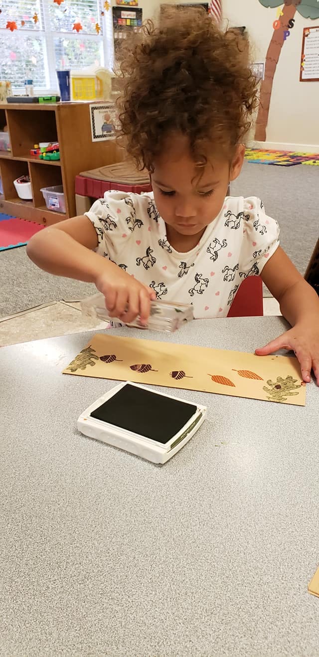 Child stamping leaf shapes onto a piece of paper in a classroom